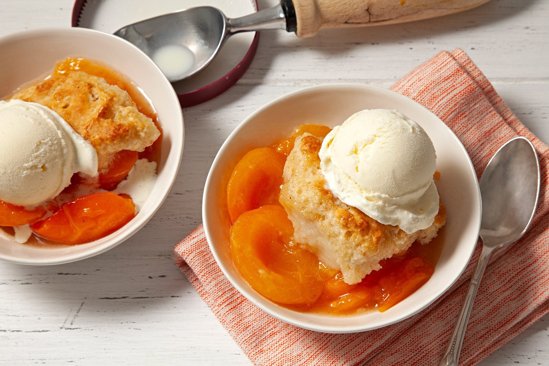 overhead shot; white background; Apricot Cobbler in two small bowls served with ice cream over kitchen towel