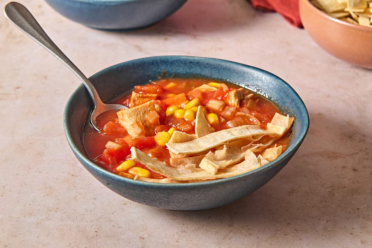 Closeup shot of a bowl of chicken tomato soup topped with tortilla strips