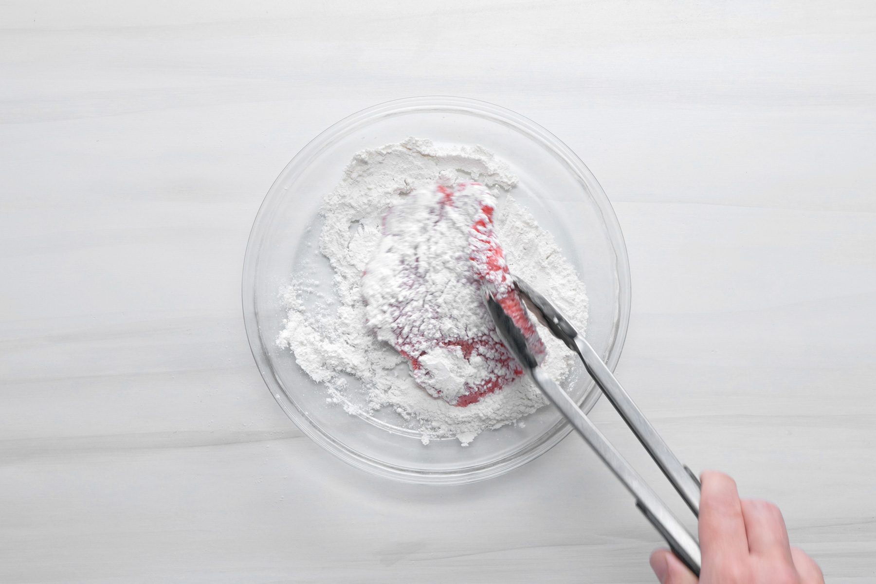 A hand is coating beef cube steaks with flour
