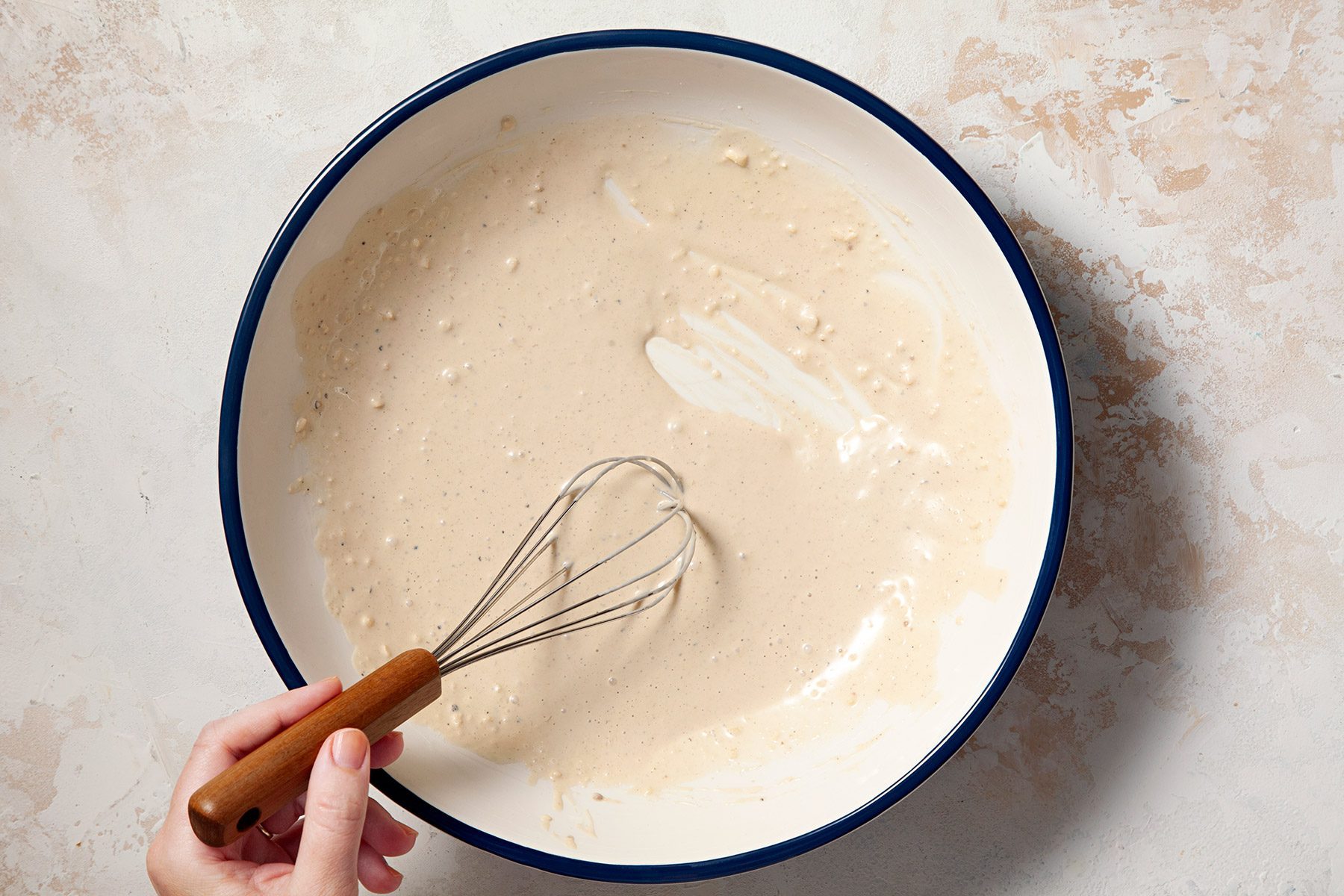 Overhead shot of same bowl; mixture; whisk tool; cream marble background