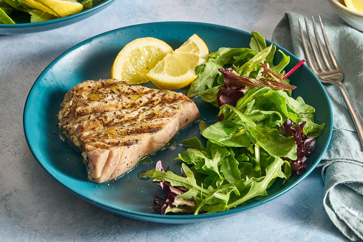 Closeup of a grilled tuna steak with salad and lemon wedges
