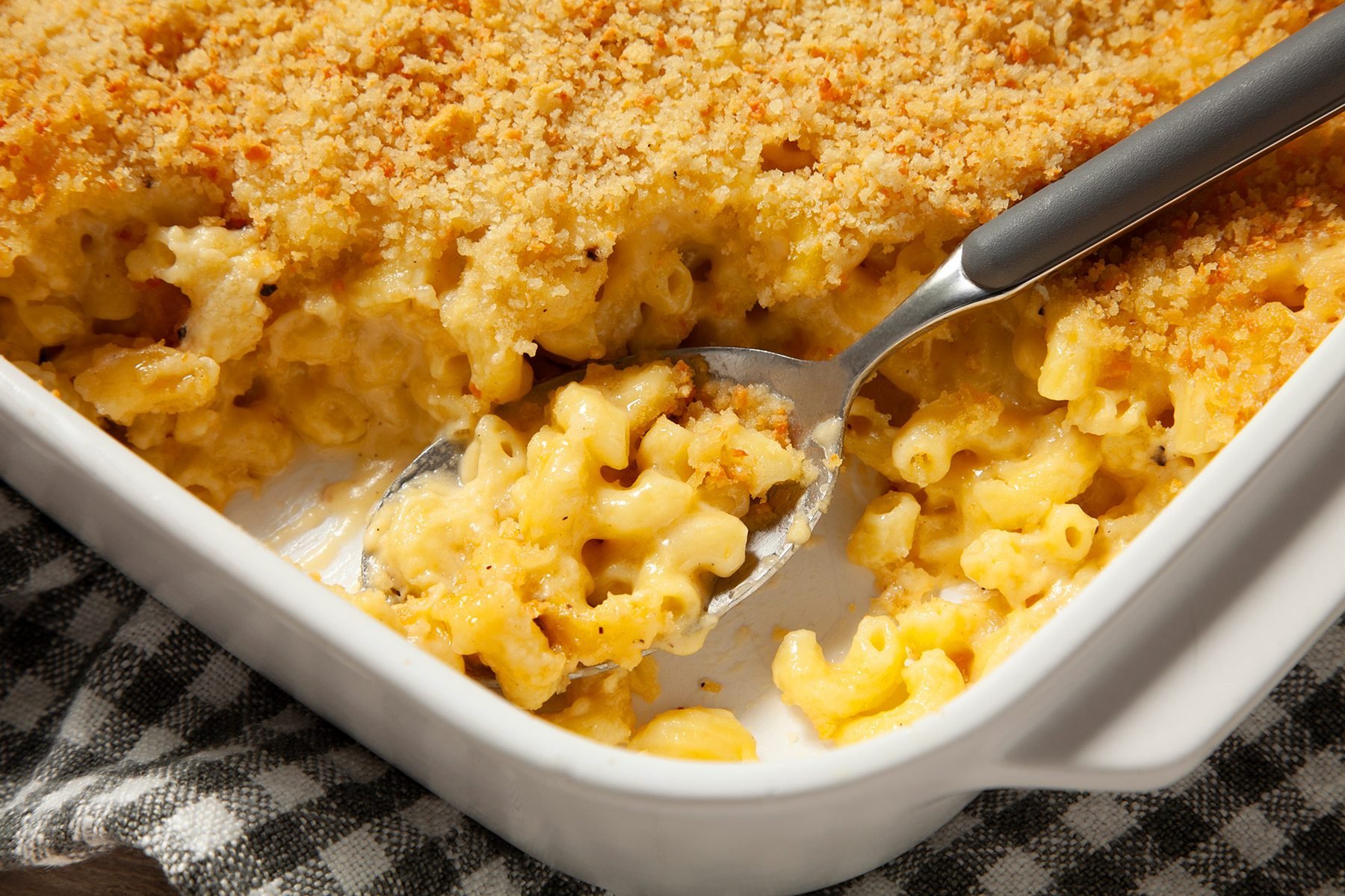 3/4th shot; close shot; wooden background; Baked Three-Cheese Macaroni in a rectangular dish over kitchen napkin with spoon inside it;