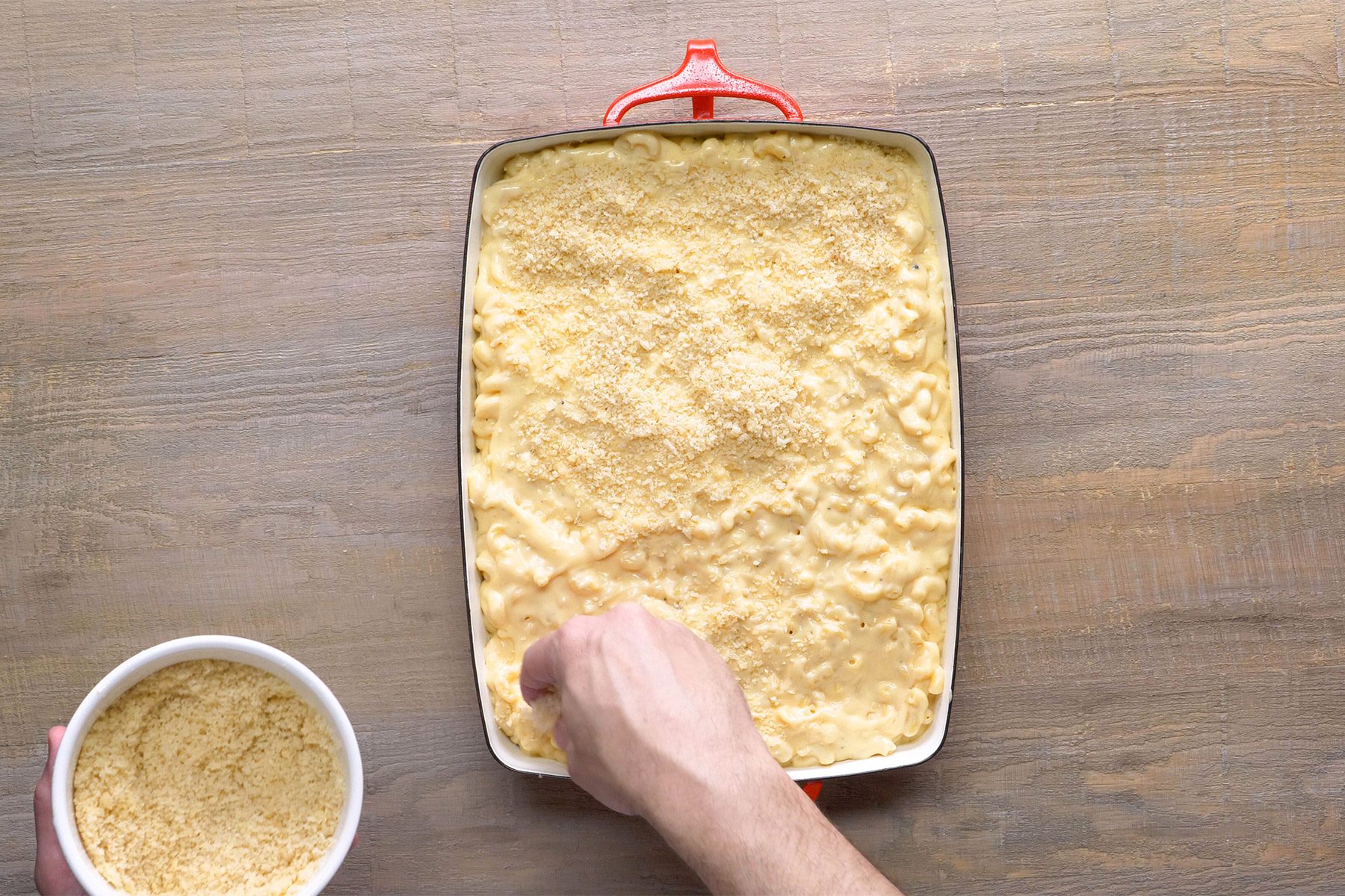 overhead shot; wooden background; placed mac and cheese into a baking dish sprinkling bread crumbs over it;