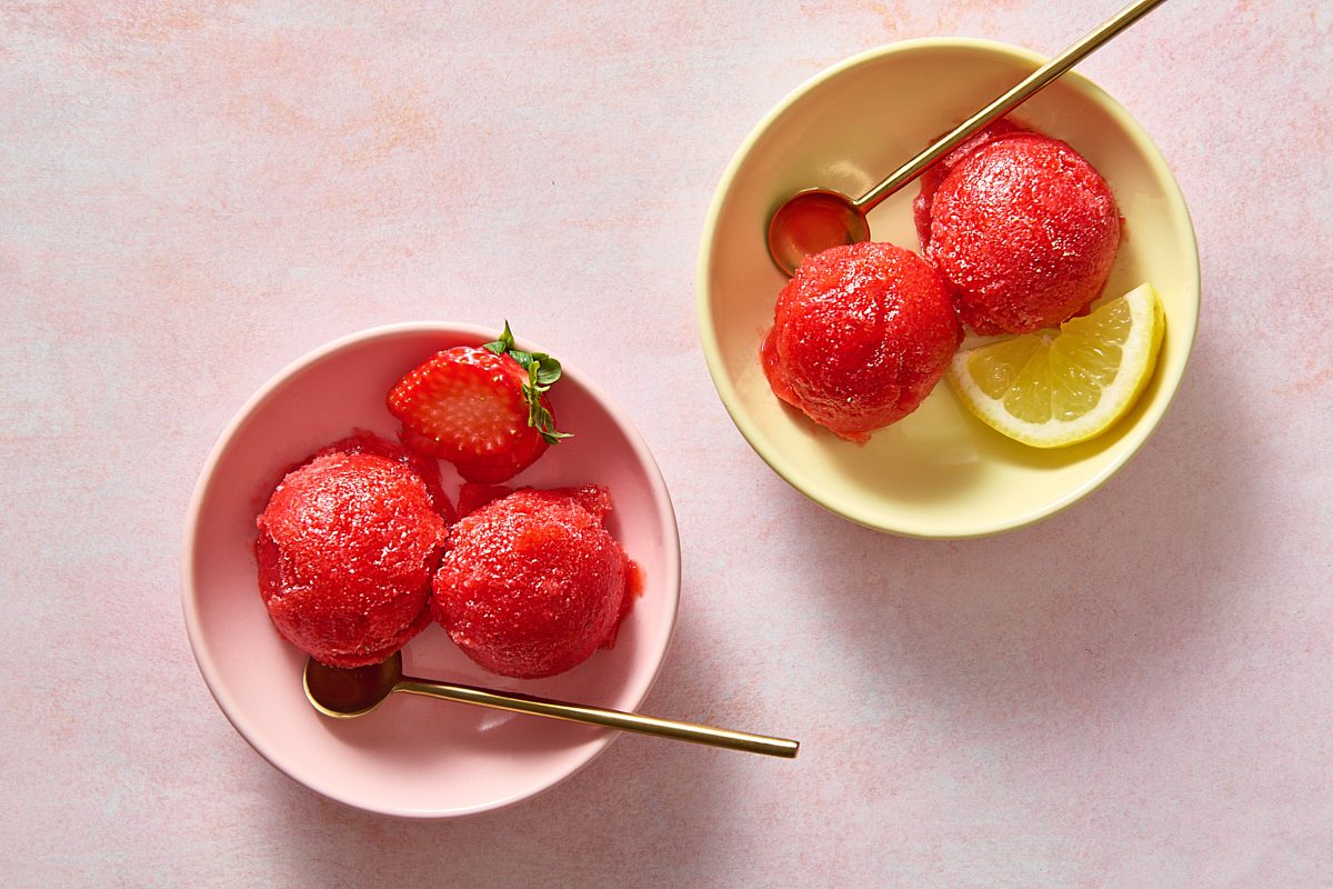 Overhead shot of two bowls of strawberry ice with spoons and garnish