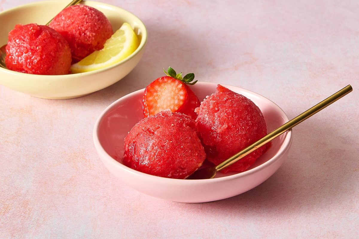 Closeup of strawberry ice in a bowl with a spoon and some fresh strawberry