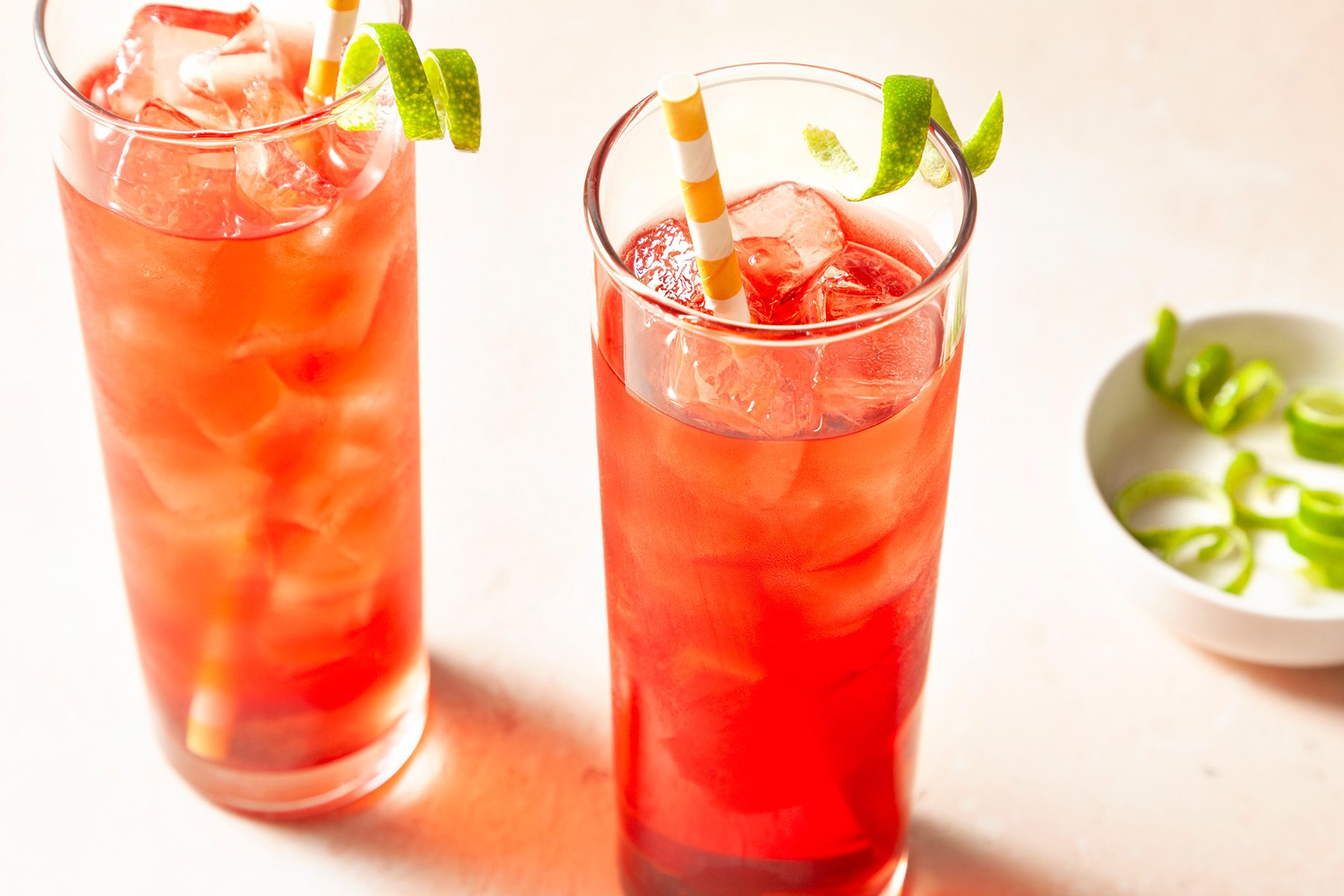 High angle view shot of Vodka Cranberry; placed ice a highball glass; poured the vodka and cranberry juice into the glassgarnished with lime twist; straws; light pink background;