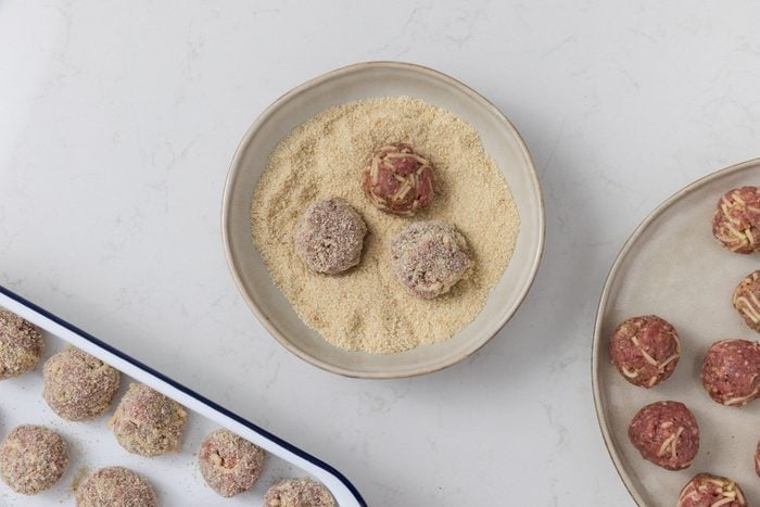 Meatballs being breaded and put into baking dish.