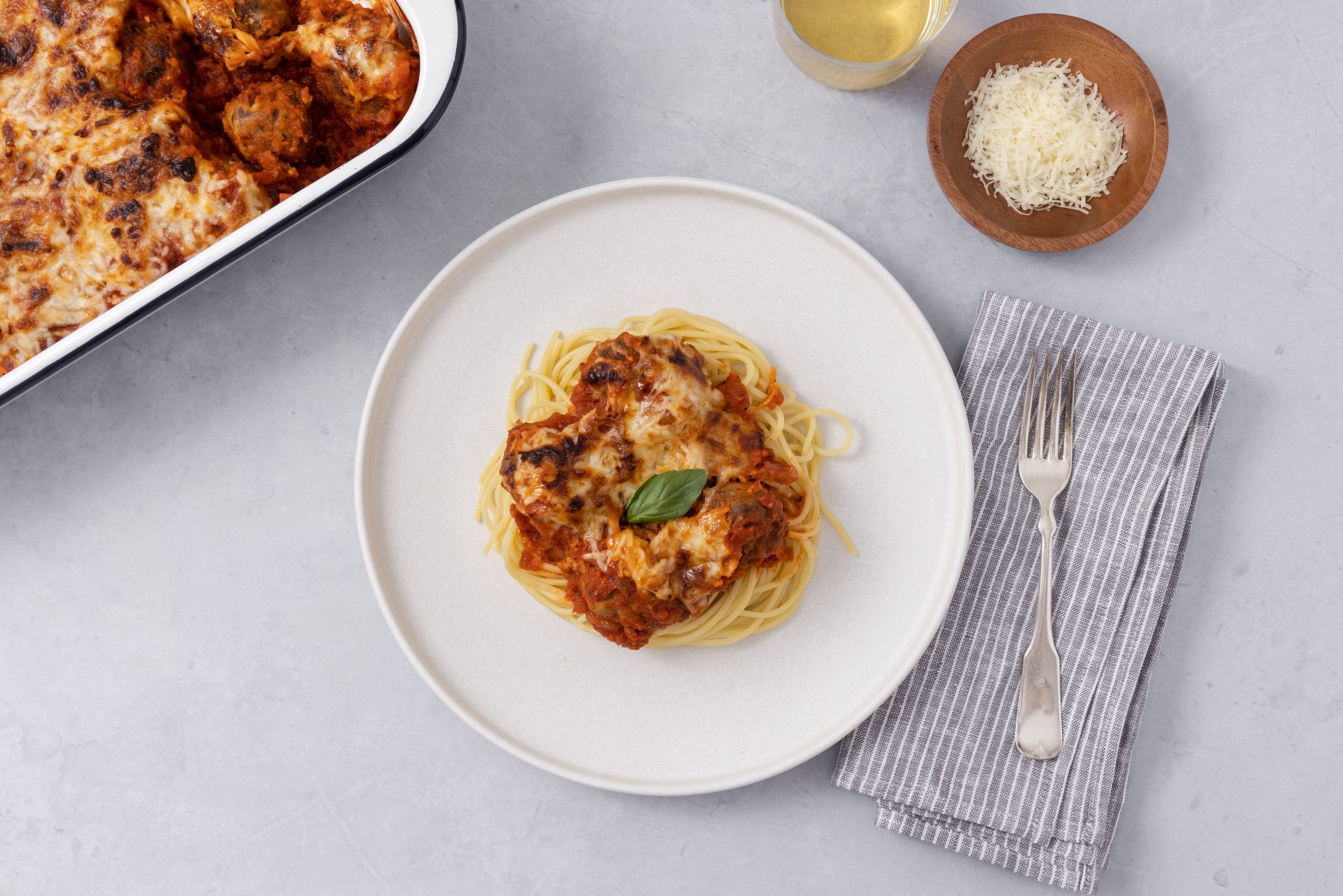 Baked meatballs served with spaghetti on a plate and baking dish on the side.