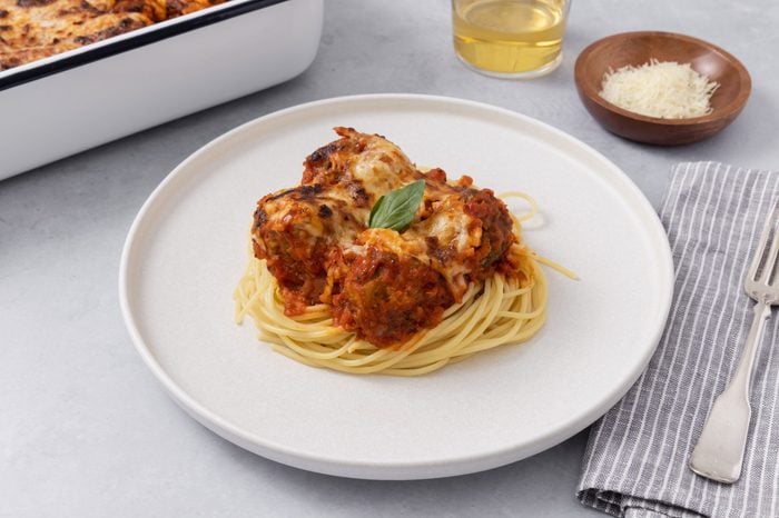 Close-up of baked meatballs served with spaghetti on a plate and baking dish in the background.