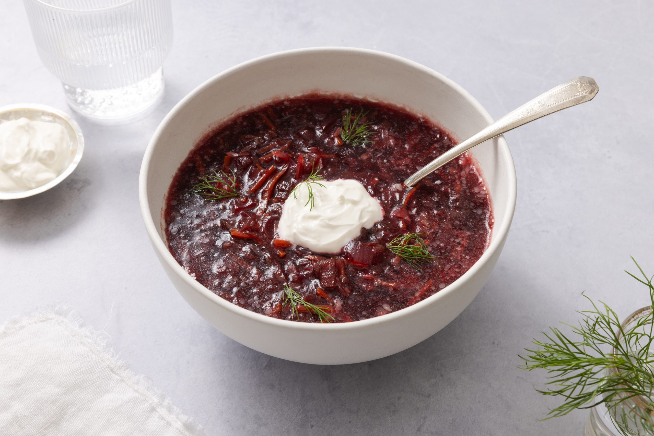 Borscht soup served in ceramic bowl garnisehd with sour cream and dill sprigs.