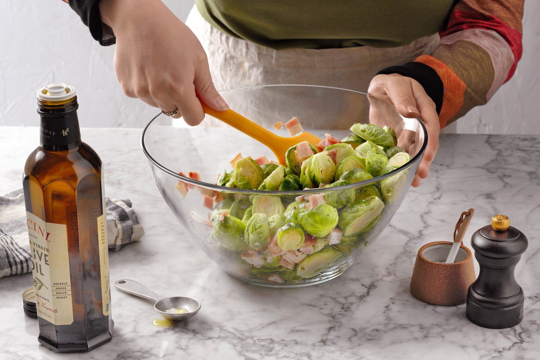 A person tossing Brussels Sprouts with Bacon and olive oil in a bowl.
