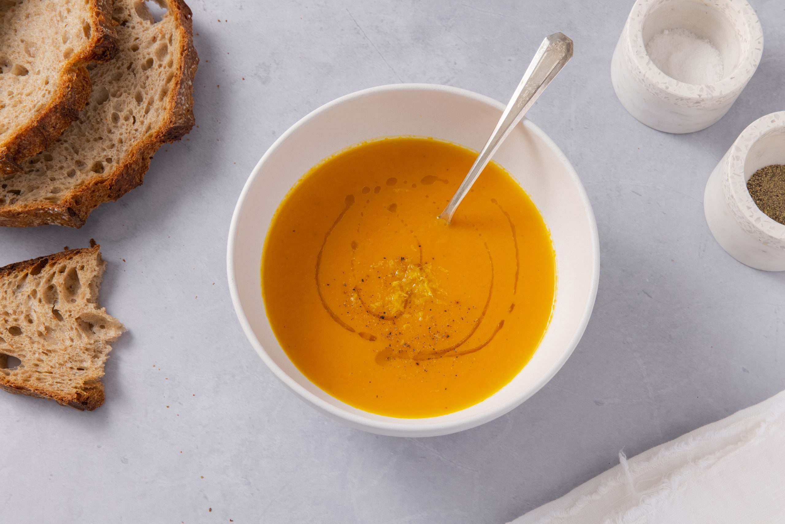 Carrot ginger soup served in bowl with spoon and bread on the side. 