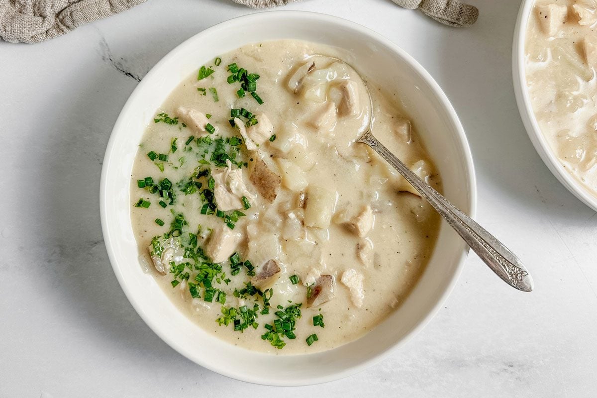 Taste of Home chicken potato soup in white ceramic bowls with a linen napkin on a marble surface.
