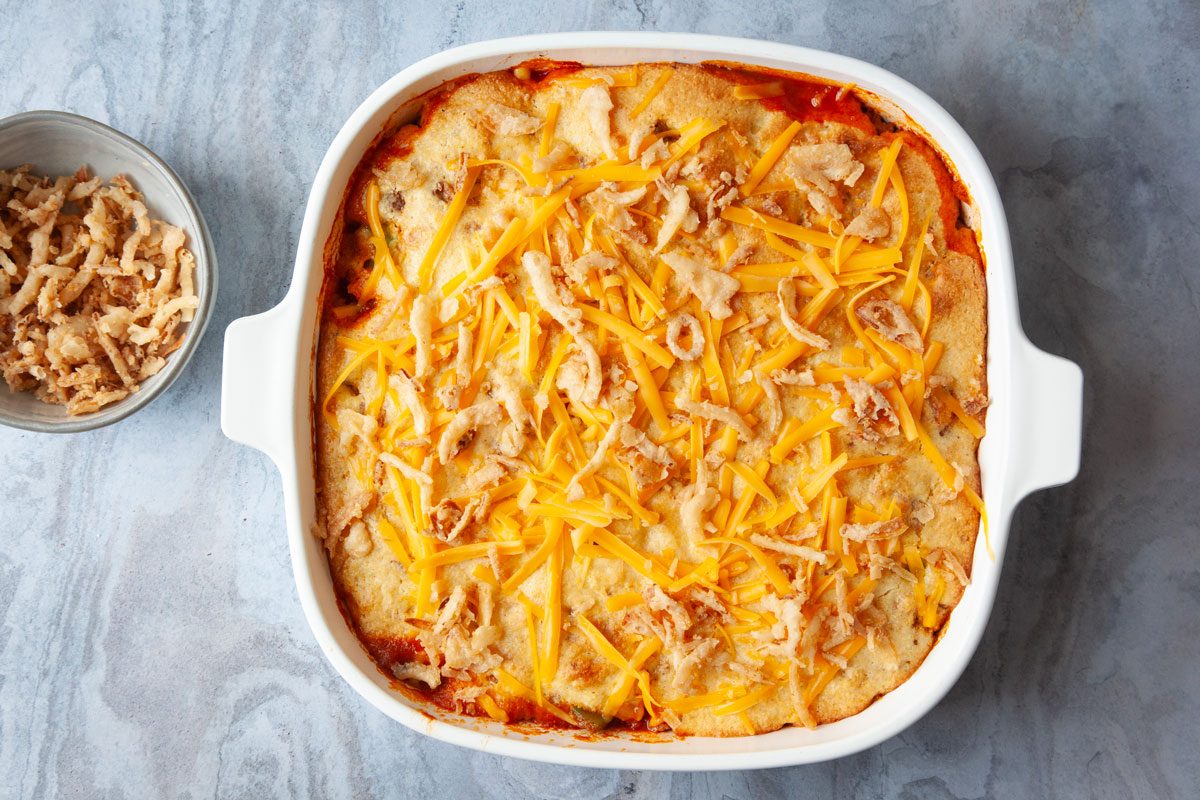 Step 3 of Taste of Home Cornbread Taco Bake is to top the baked casserole with the remaining french fried onions and cheddar cheese