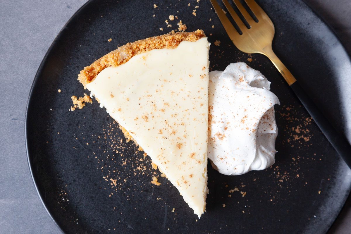 Single serving of Taste of Home Eggnog Cheesecake on a black plate with whipped cream and nutmeg