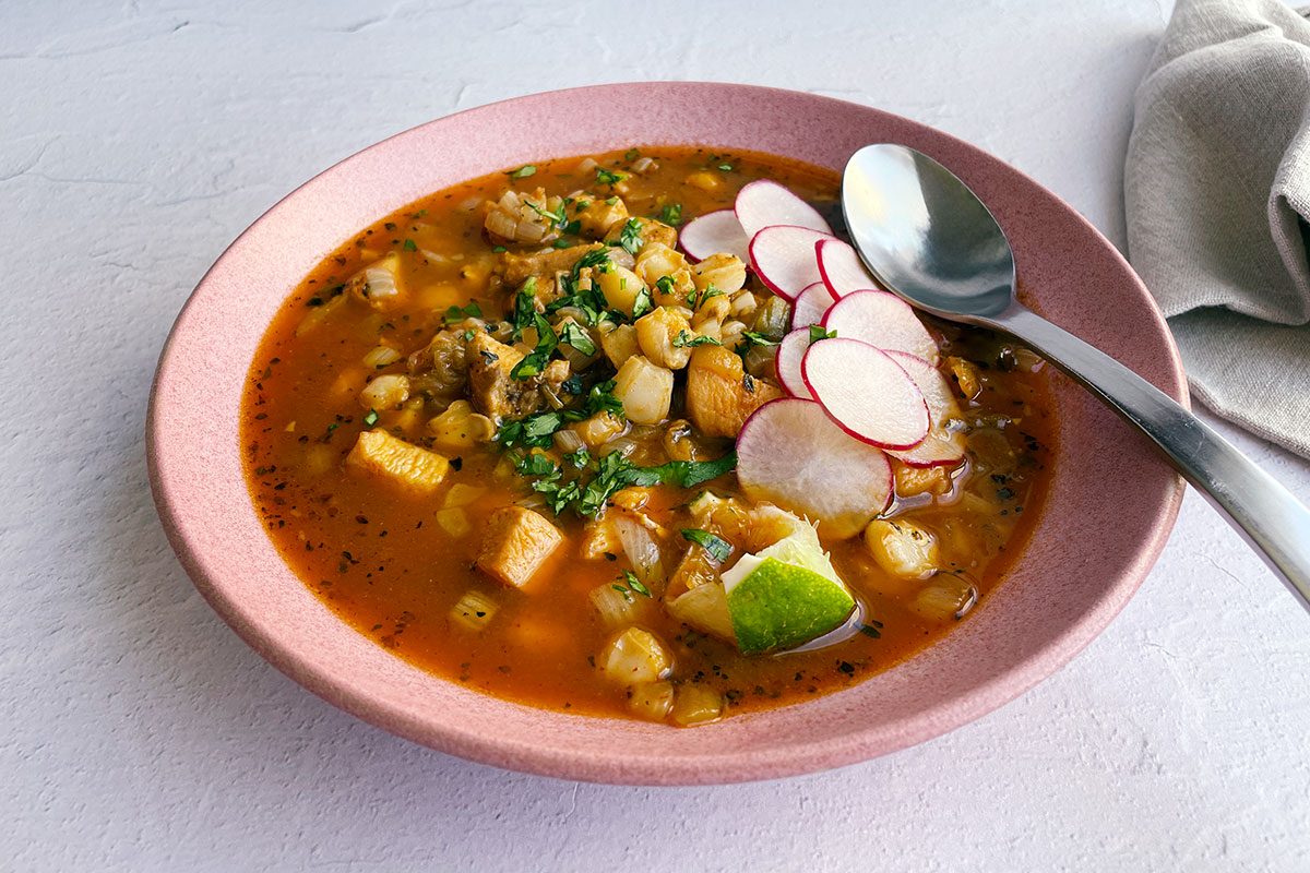Taste of Home's Hominy Soup in a pink bowl on a white tile background