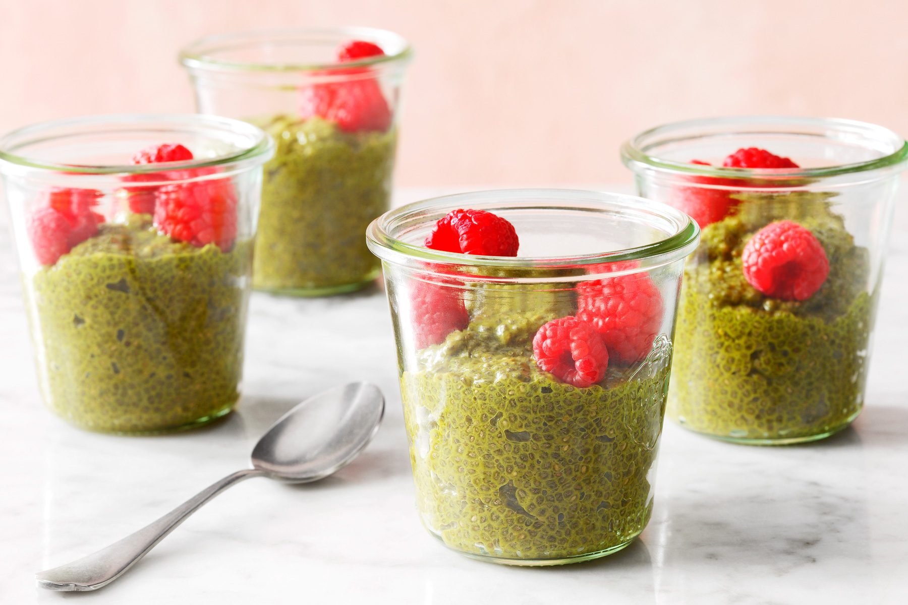 Four cups of Matcha Chia Pudding on a counter top and a spoon among them