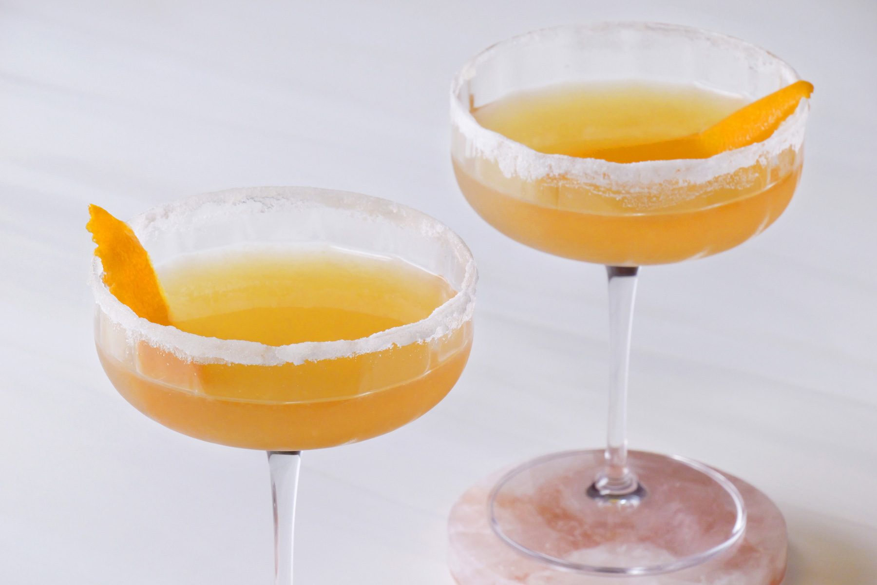 Two glasses of sidecar cocktail with orange peel on a coaster