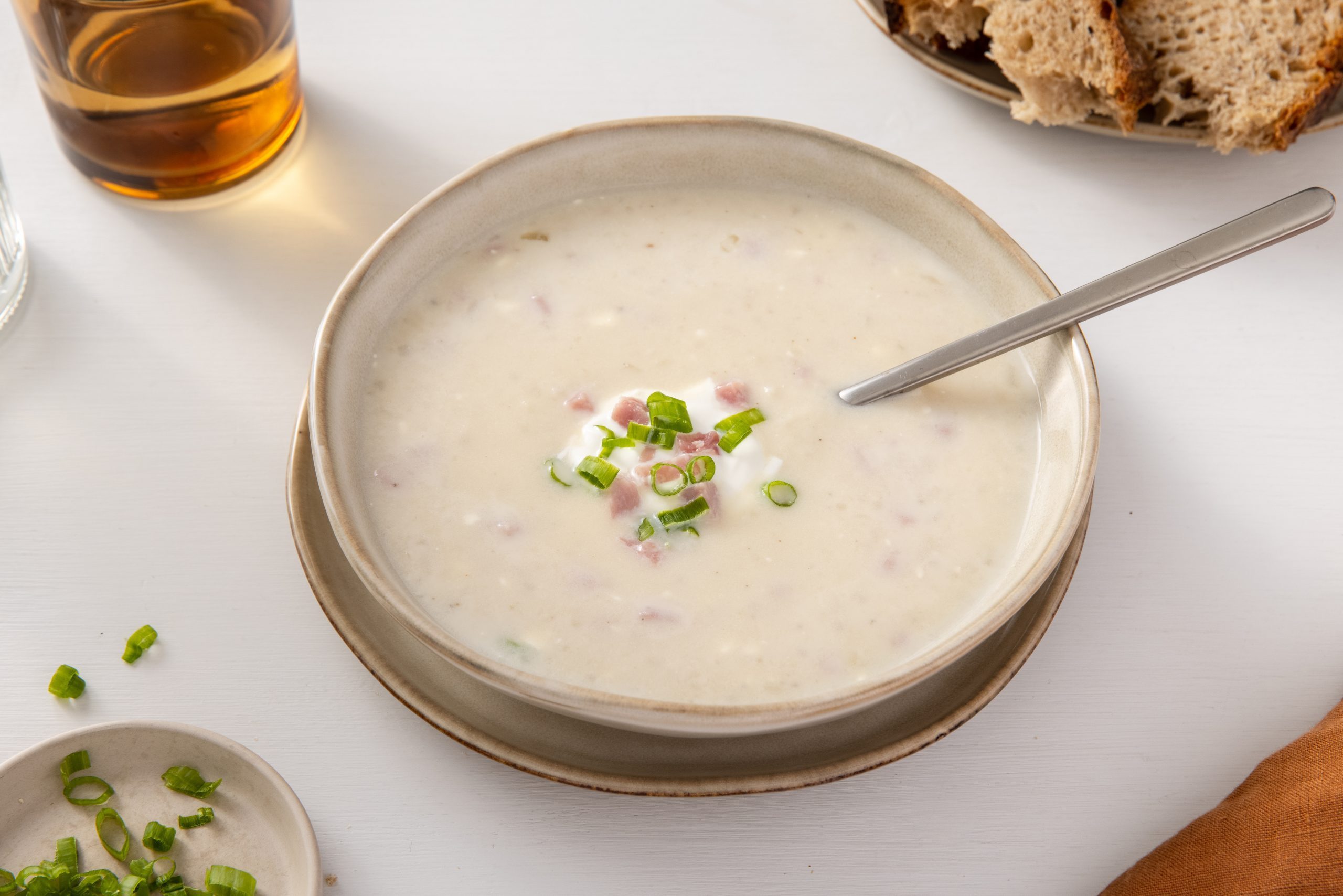 Soup ready served in bowl garnished with green onions, sour cream and ham. 