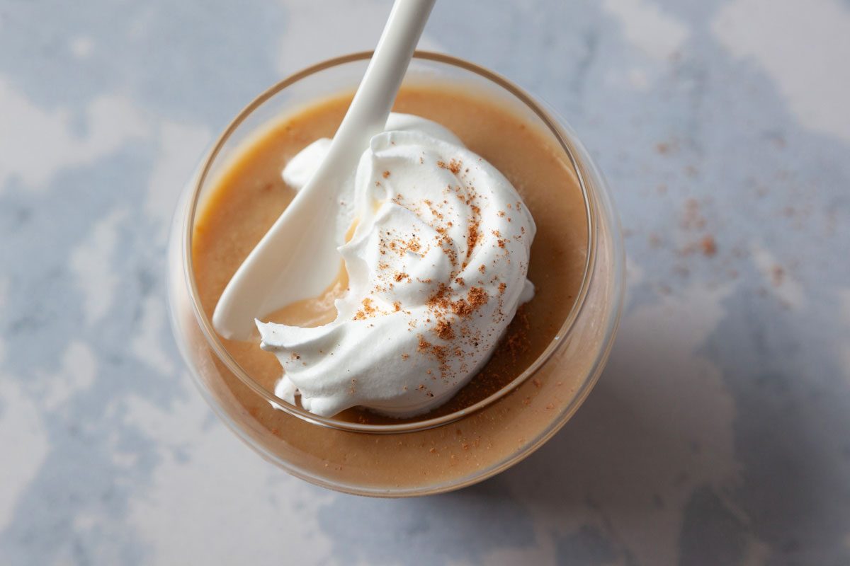 Close up overhead of one single servings of Butterscoth pudding with whipped cream and ground nutmeg in dessert dishes with a white spoon