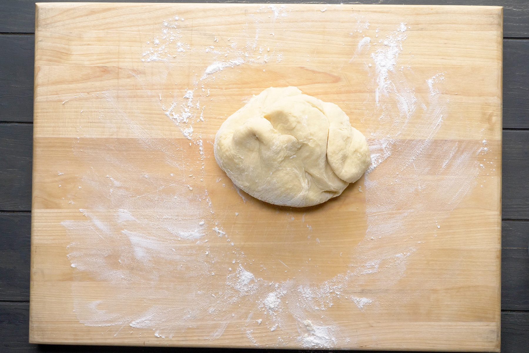 A ball of dough rests on a wooden surface dusted with flour. 