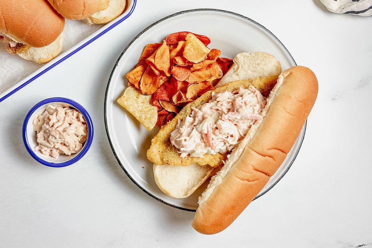 Taste of Home Catfish Po'boy on enamel tray and plate next to a striped napkin on a marble surface.