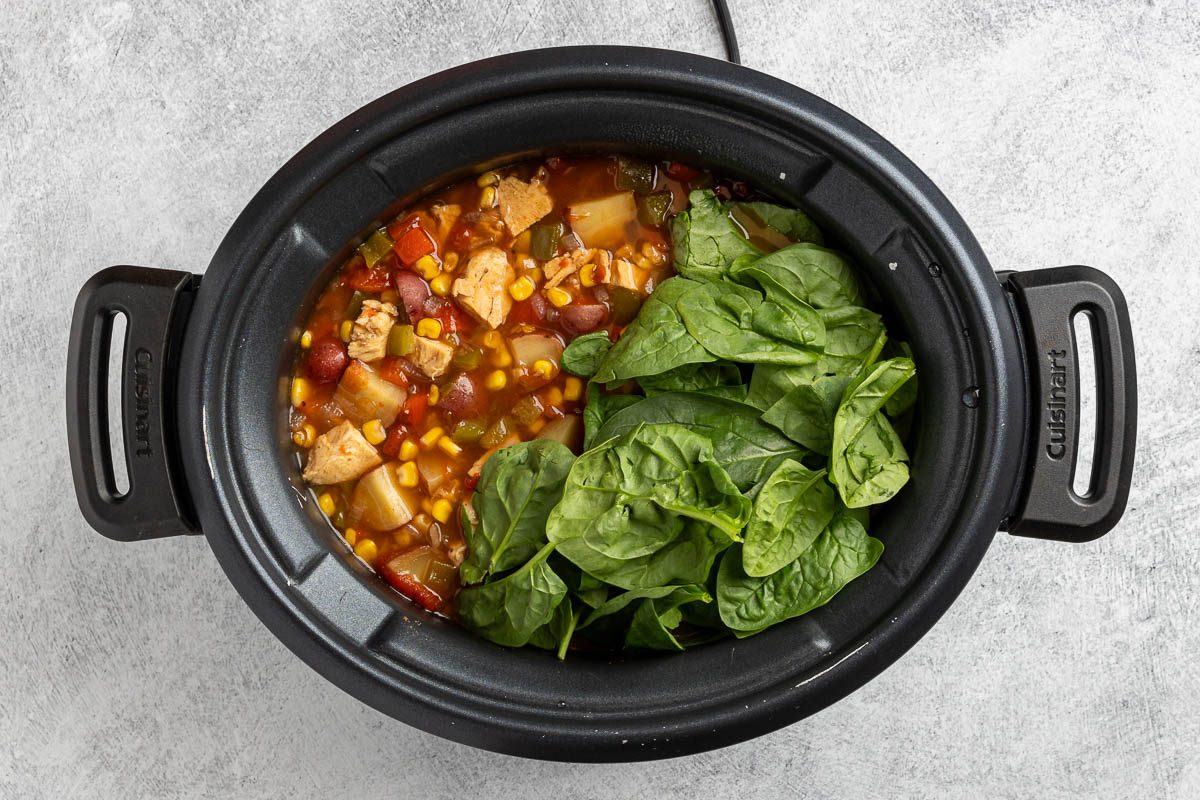 Taste of Home Crockpot Chicken Vegetable Soup recipe photo of the cooked soup with the fresh spinach added to the crockpot.
