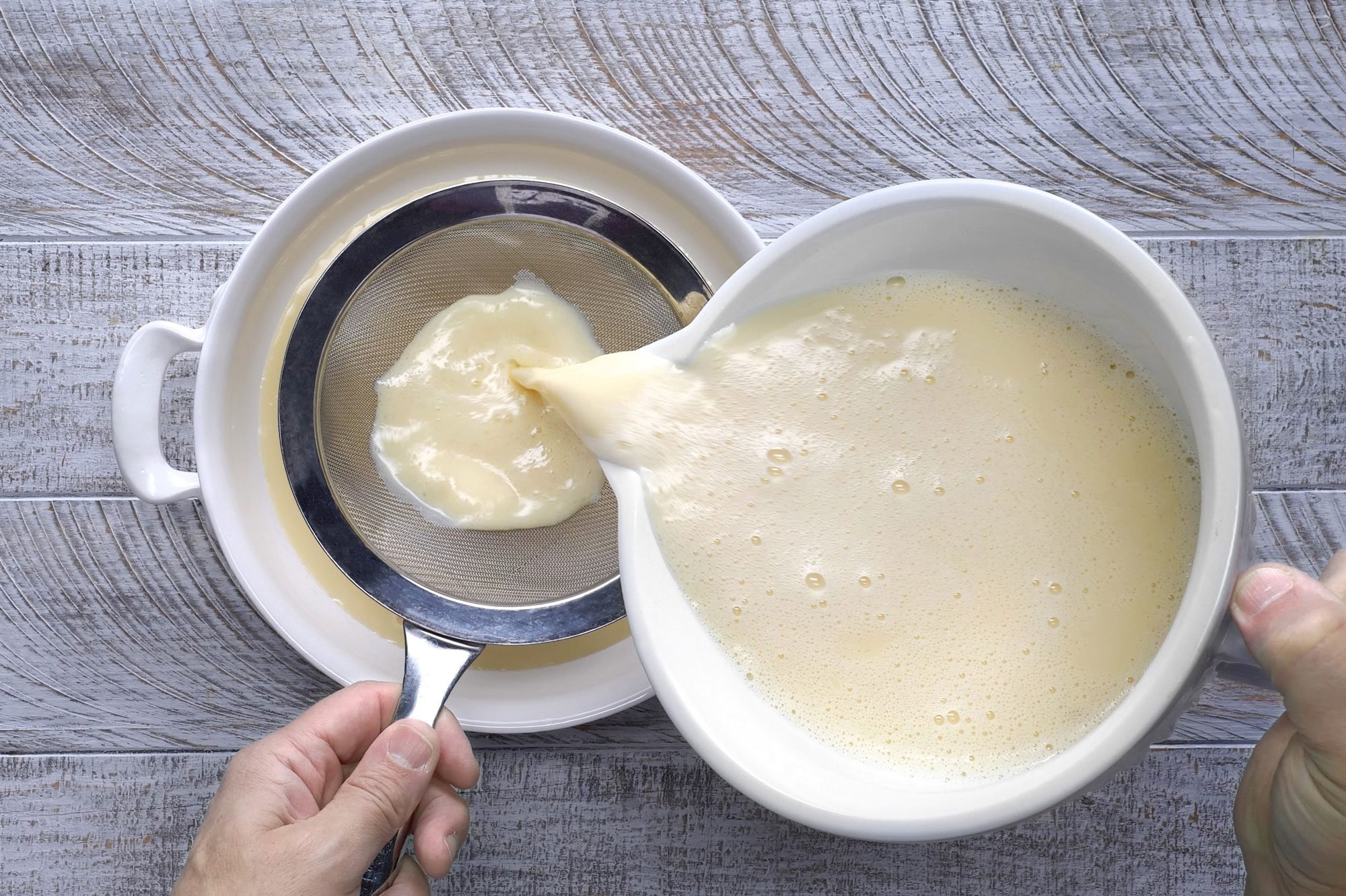 Overhead shot of pour egg mixture through a strainer into a round baking dish; wooden background;