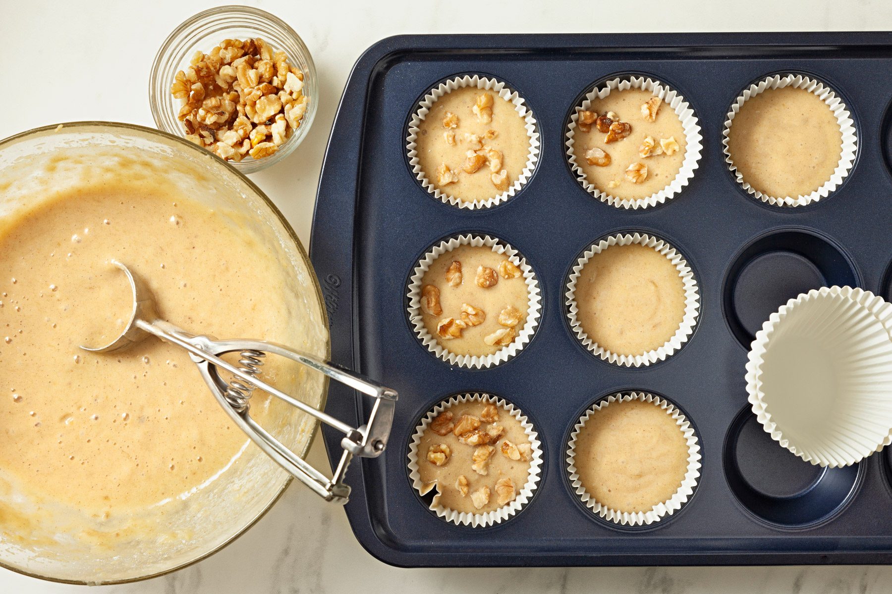 Muffin cups lined with paper are being filled with batter.