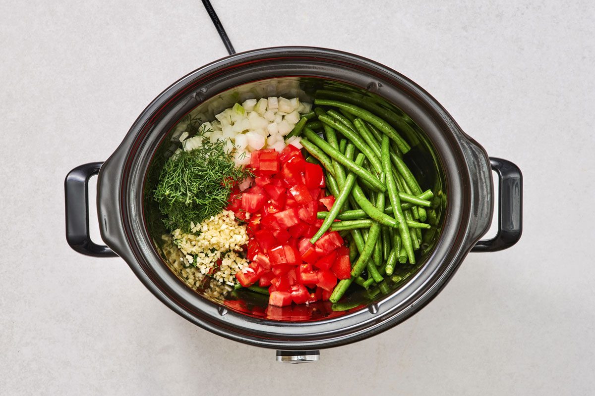Combining the green beans, tomatoes, onion, broth, dill, lemon juice and garlic in a quart slow cooker