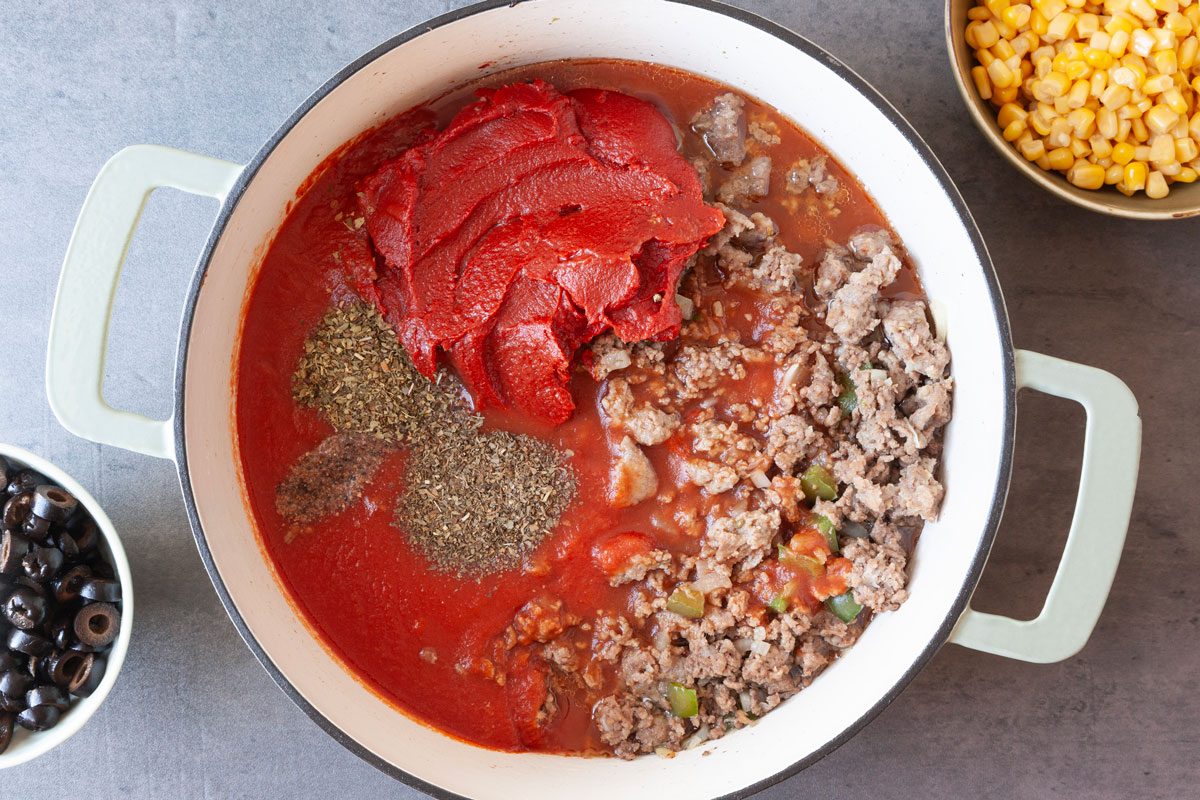 Step 2 of Taste of Home Italian Casserole is to add the tomato sauce, tomato paste, water and seasonings to the Dutch oven, and bring the liquid to a boil. Reduce the heat, then cover and simmer for 15 minutes. Add the corn and olives, then cover the Dutch oven and simmer for an additional five minutes. Stir in the cooked noodles.