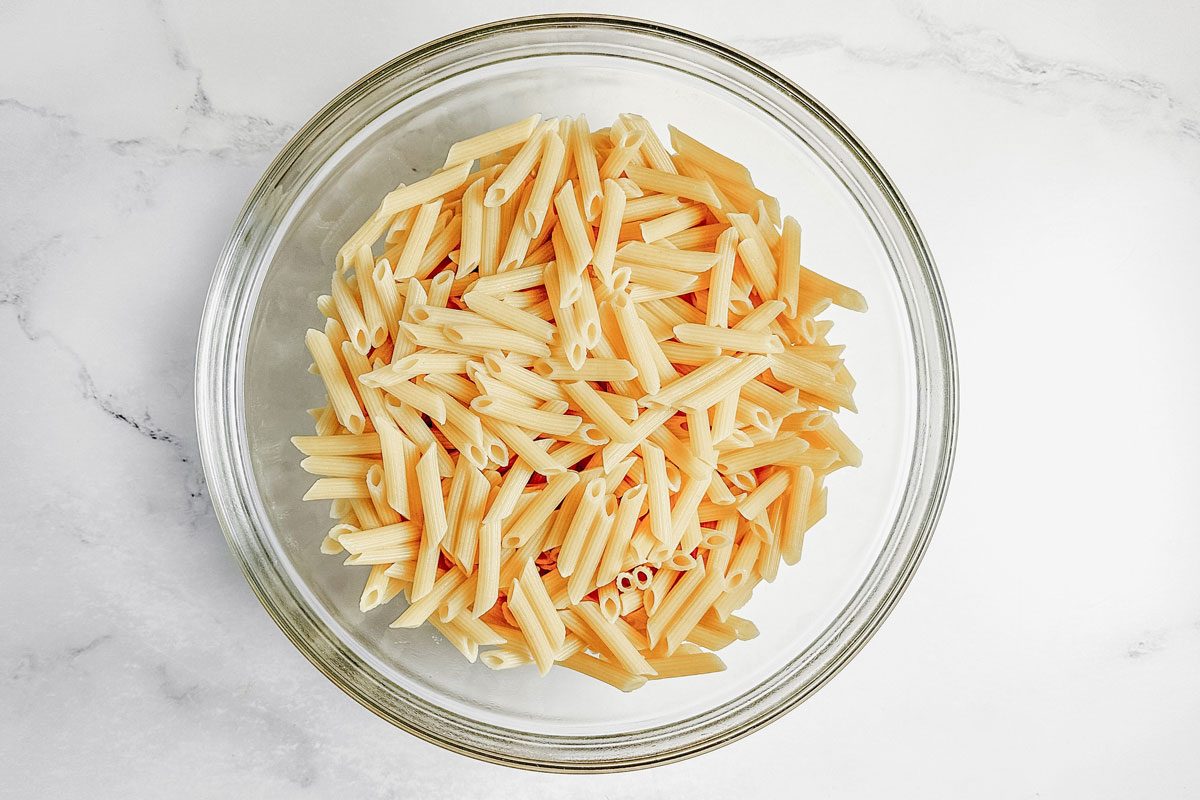 Cooked and drained penne in a glass bowl for Taste of Home kielbasa casserole.