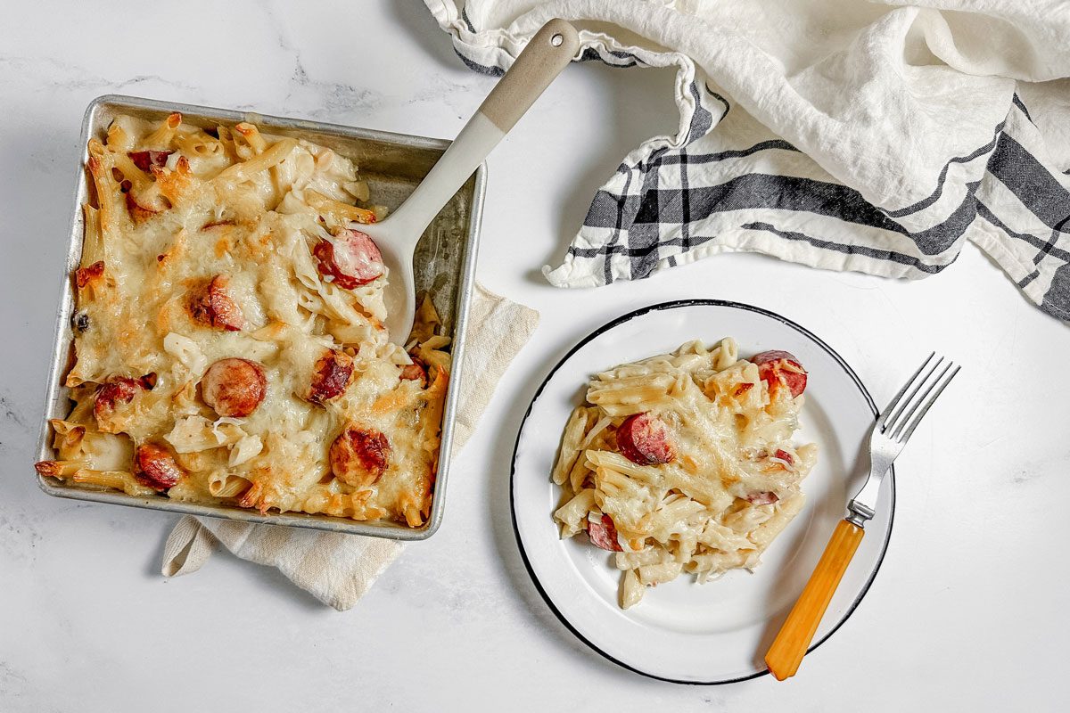 Taste of Home kielbasa casserole on an enamel plate next to a baking dish with kielbasa casserole.