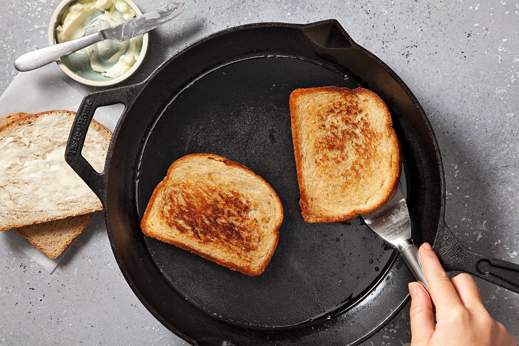 overhead shot; grey textured background; in a skillet, buttered side down, and toasting bread until lightly browned