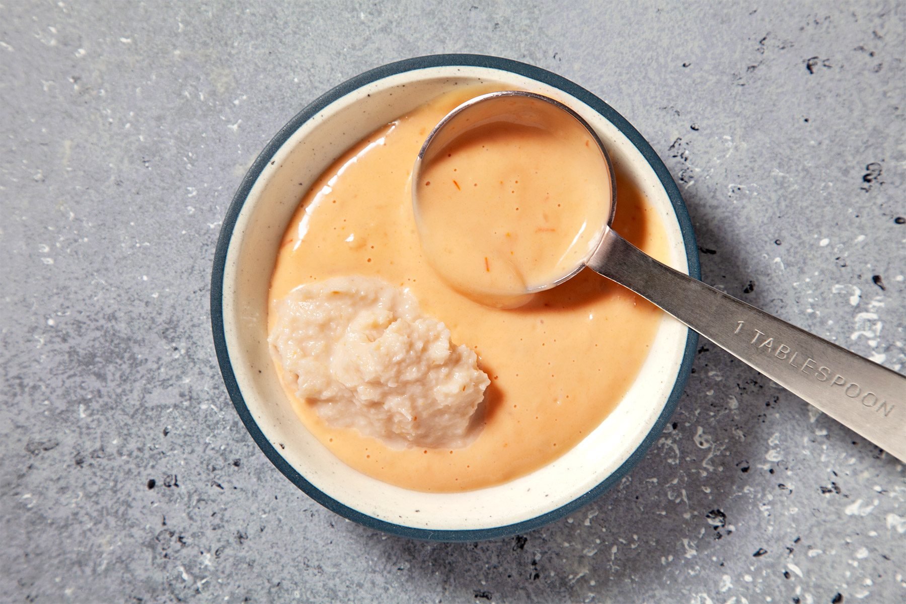 overhead shot; grey textured background; Combining salad dressing and horseradish with measuring spoon;