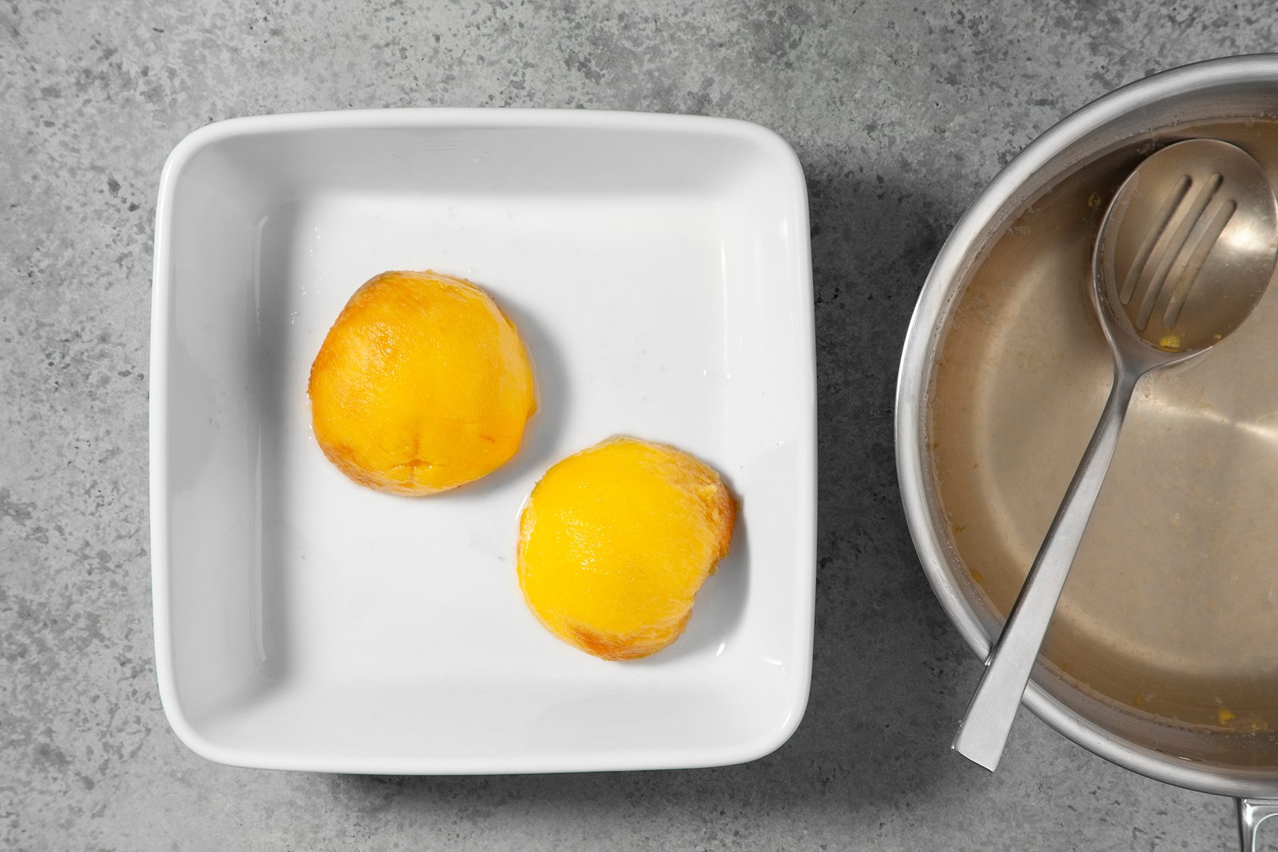 A white rectangular dish holds two round, golden-brown pastries. Beside it, a round metallic bowl with a ladle rests on a grey countertop.