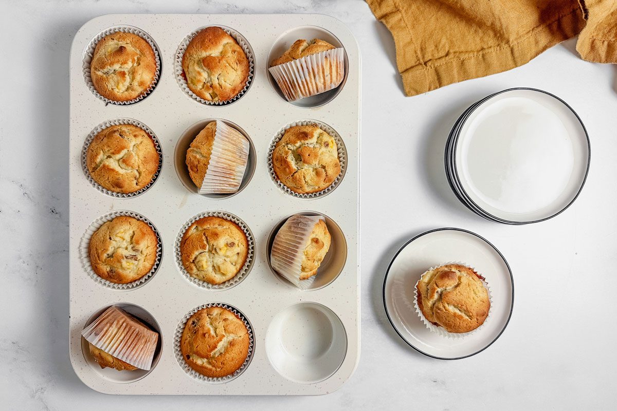 Taste of Home peach muffins in muffin tins and a white plate on a marble surface.