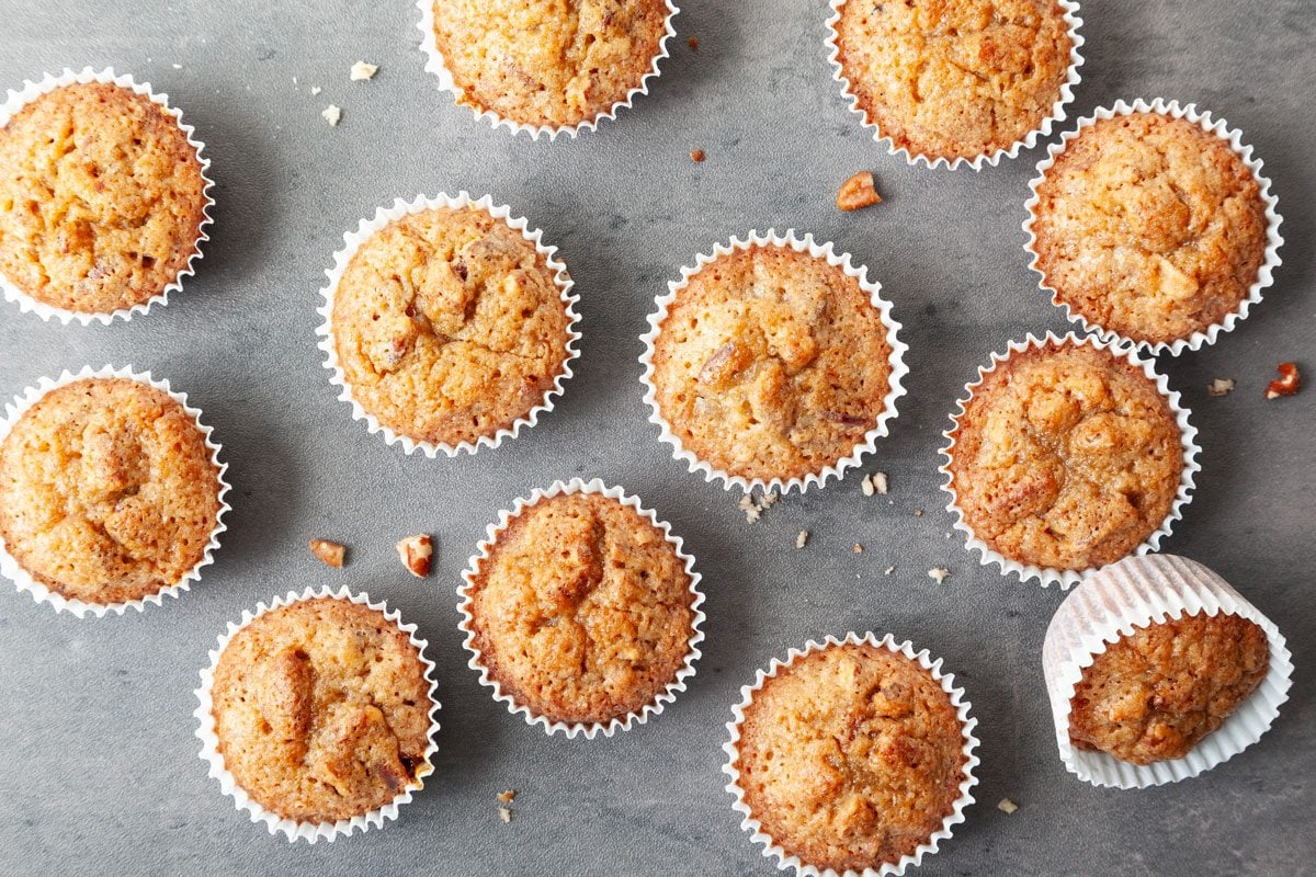 Full yield of Taste of Home Pecan Pie Muffins on a black surface, scattered with pecan pieces