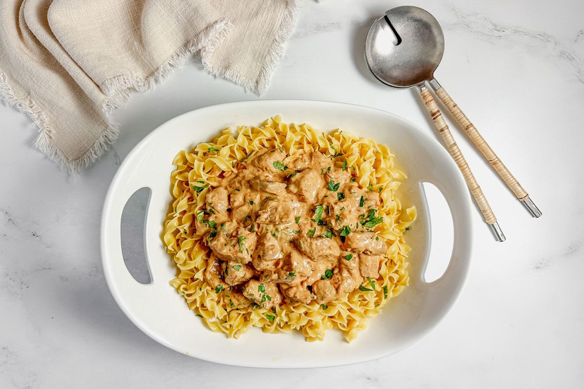 Taste of Home pork stroganoff in a white ceramic bowl with a cloth napkin on a marble surface.