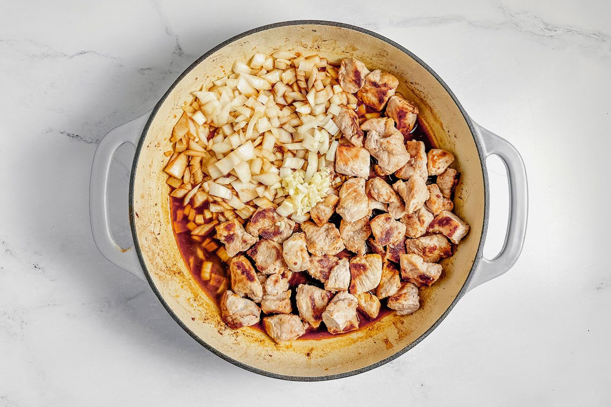 Ingredients for Taste of Home pork stroganoff in a ceramic skillet on a marble surface.