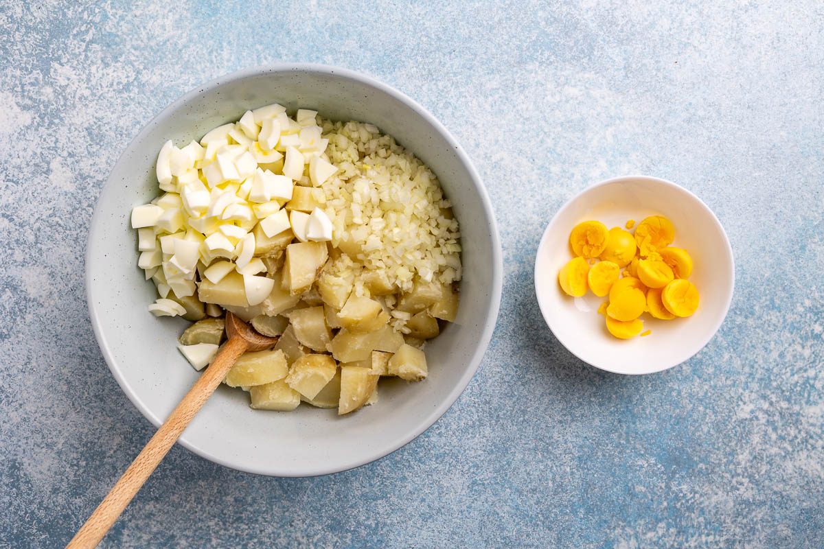 Taste of Home Potato Salad Recipe photo of potatoes and other ingredients in a mixing bowl with with a bowl of hard boiled egg yokes on the side.