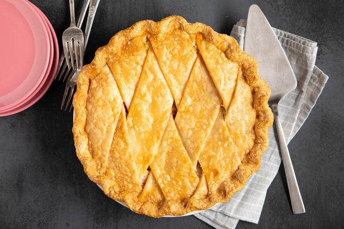 An overhead view of a freshly baked Rhubarb Custard Pie with plates, forks, and a pie server.