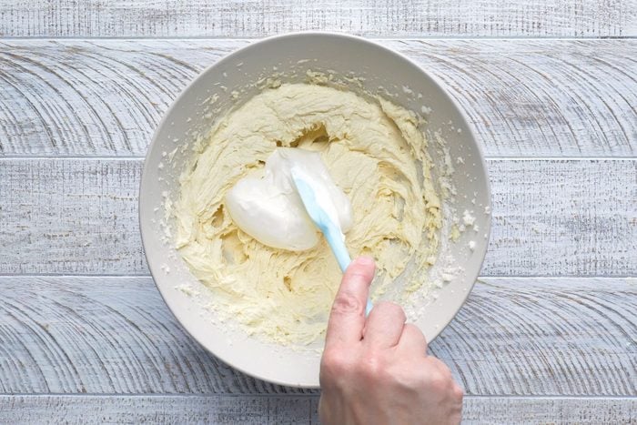 Sour cream is being added with a spatula to a mixture of flour, baking soda and salt.