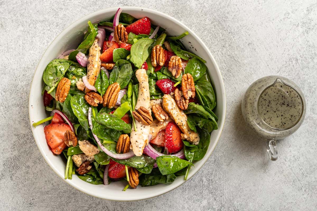 Taste of Home Strawberry Chicken Salad recipe photo of the tossed salad topped with pecans with additional dressing.