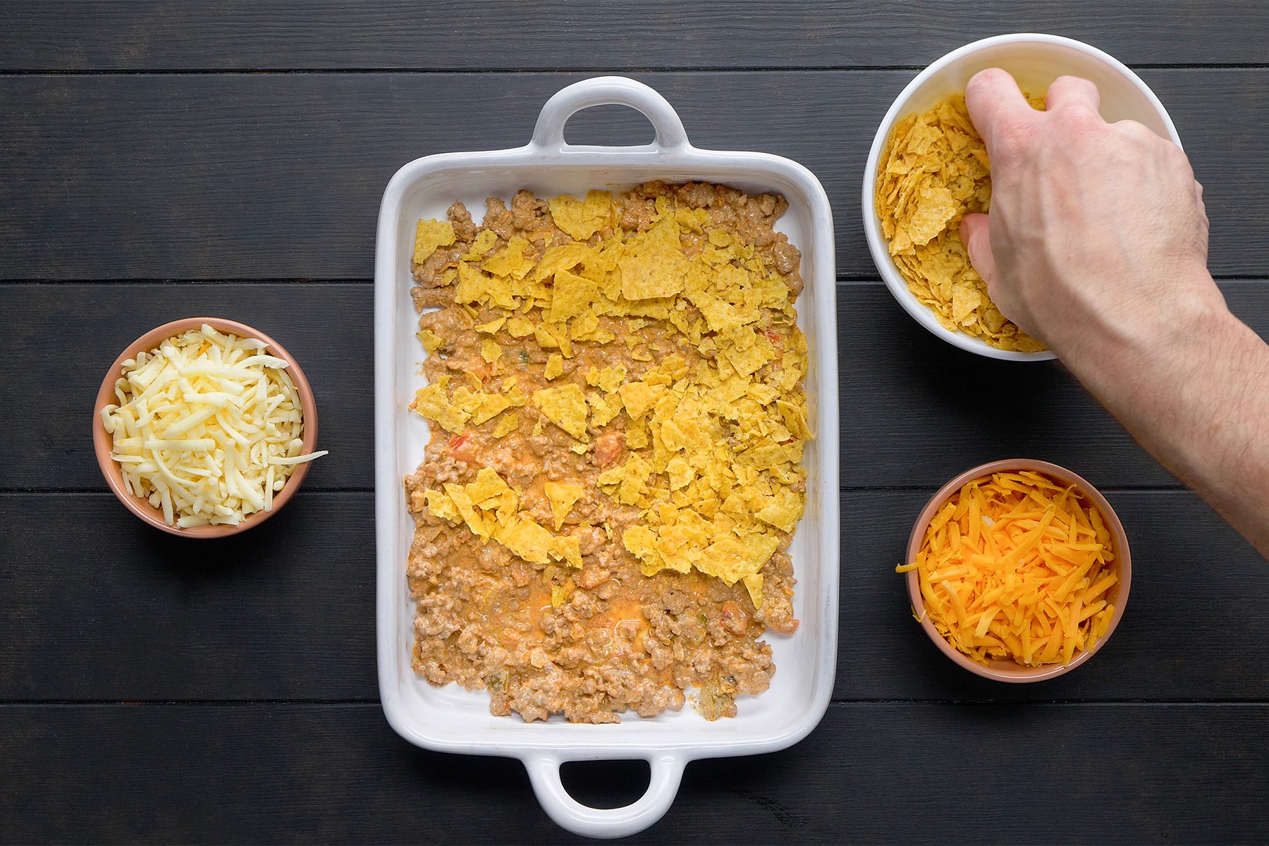 overhead shot; black background; In an baking dish, layering half of the meat mixture with chips and cheeses;