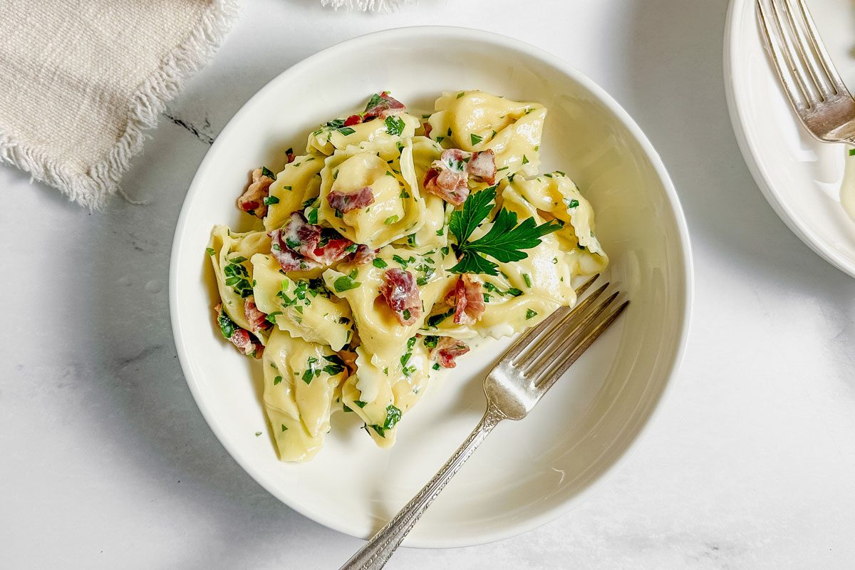 Taste of Home tortellini carbonara in white ceramic bowls with a linen napkin on a marble surface.