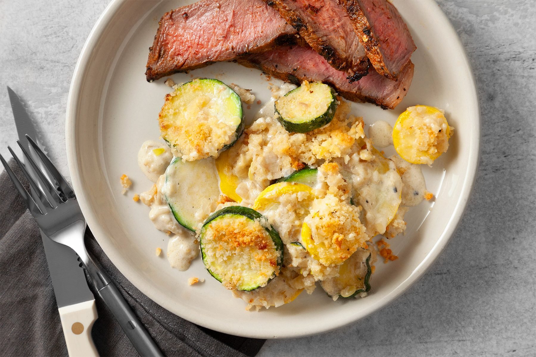 wide shot of yellow squash and zuchhine gratin served with steaks