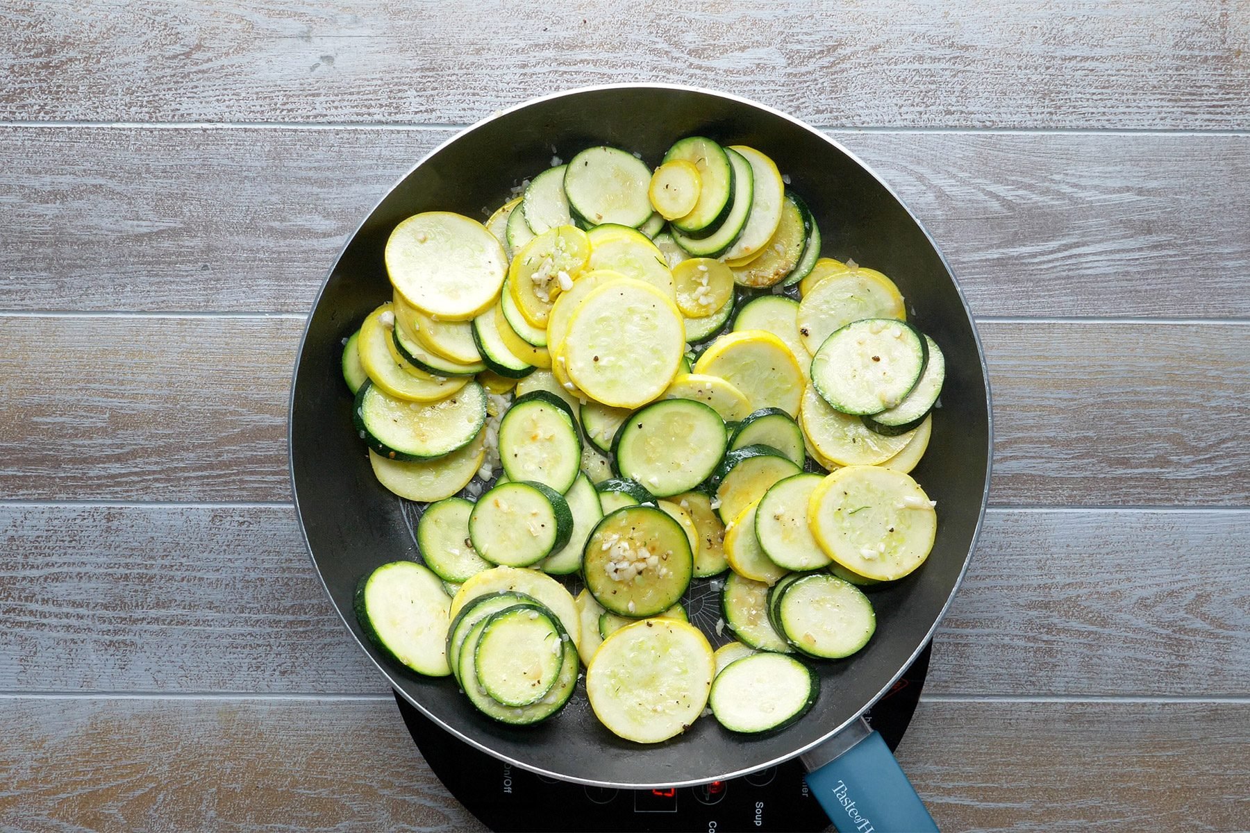 overhead shot of sliced zucchini, yellow squash and shallots in a large skillet