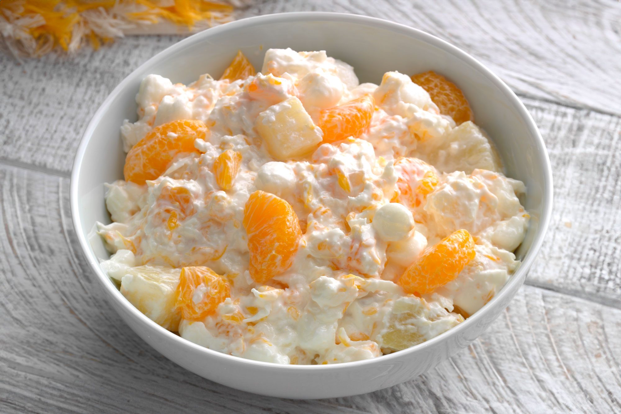 3/4th shot of Ambrosia Salad in a large bowl; wooden background;