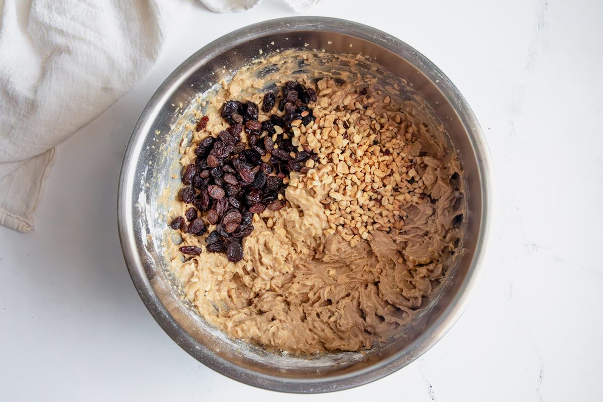 Raisins and mixed nuts in unmixed cookie batter for Taste of Home Apple Butter Cookies on a marble surface.